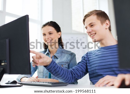 education, technology, school and people concept - two smiling students having discussion in computer class at school