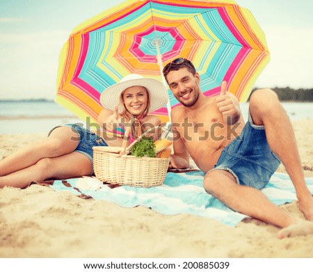 summer, holidays, vacation and happy people concept - smiling couple lying on the beach under colorful umbrella and showing thumbs up