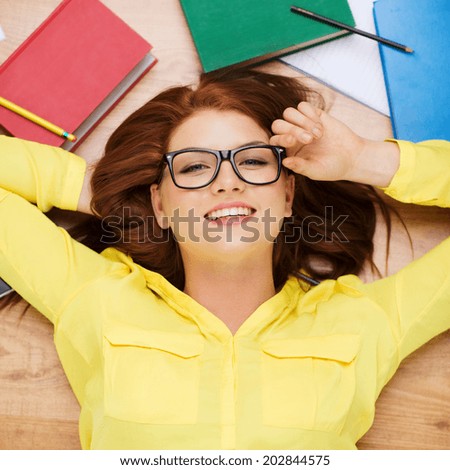 education and home concept - smiling redhead female student in eyeglasses lying on floor