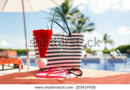 beach, summer, christmas, holidays and vacation concept - close up of santa helper hat, flip-flops, bag, sunscreen and sunglasses at pool