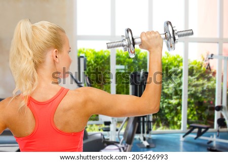 fitness, healthcare and exercise concept - young sporty woman with heavy steel dumbbell from the back