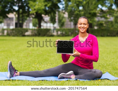 fitness, park, technology and sport concept - smiling african american woman with tablet pc computer sitting on mat outdoors