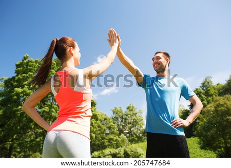 fitness, sport, training and lifestyle concept - two smiling people making high five outdoors