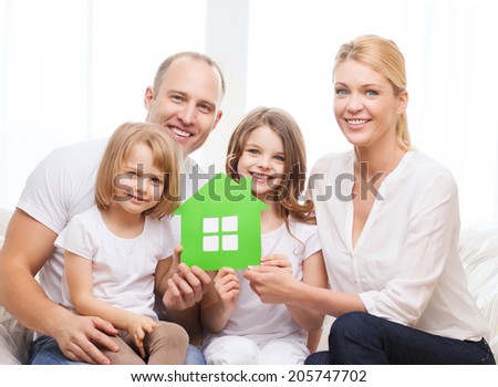 real estate, family, children and home concept - smiling parents and two little girls holding green house