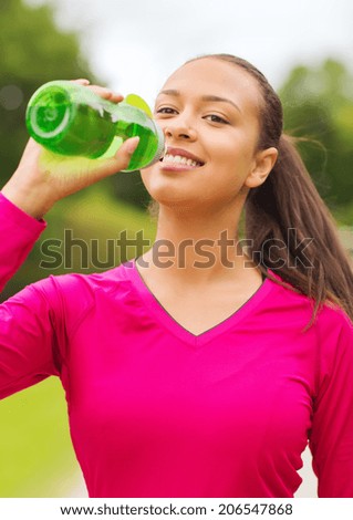 fitness, park, drink and sport concept - smiling african american woman drinking from bottle outdoors