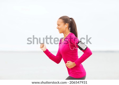 sport, fitness, health, technology and people concept - smiling young african american woman running with smartphone and earphones outdoors