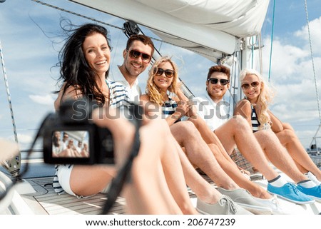 vacation, travel, sea, friendship and people concept - smiling friends sitting on yacht deck and photographing
