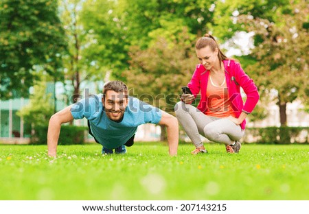 fitness, sport, training, technology and lifestyle concept - smiling man with personal trainer doing exercise outdoors