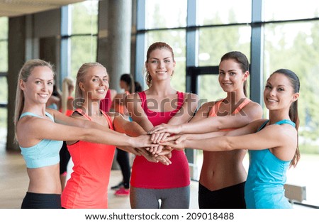 fitness, sport, friendship and lifestyle concept - group of women with hands on top of each other in gym
