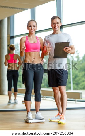 sport, fitness, lifestyle and people concept - smiling man and woman with scales and clipboard showing thumbs up in gym