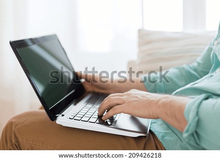 technology, leisure, advertisement and lifestyle concept - close up of man working with laptop computer and sitting on sofa at home