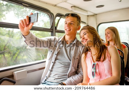 friendship, travel, summer vacation, technology and people concept - smiling couple with smartphone traveling by tour bus and making selfie