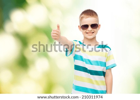 happiness, summer, childhood, gesture and people concept - smiling cute little boy in sunglasses over green background showing thumbs up