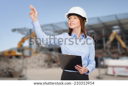 building, developing, construction and architecture concept - smiling businesswoman in white helmet with clipboard pointing finger