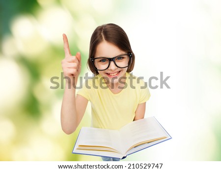 education and school concept - smiling little student girl in eyeglasses with book and finger up