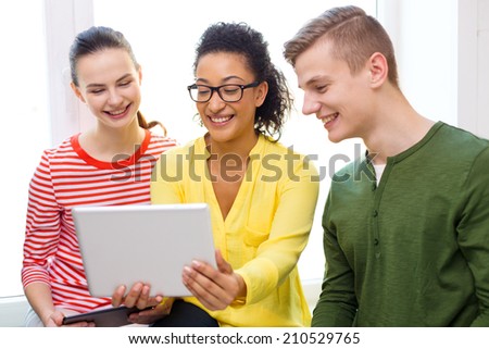 education, technology and internet concept - smiling students looking at tablet pc computer at school