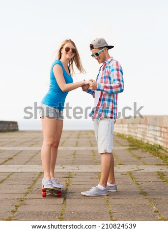holidays, vacation, love and friendship concept - smiling couple with skateboard riding outdoors