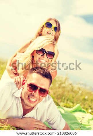 summer holidays, family, child and happy people concept - smiling family in sunglasses lying on blanket outdoors