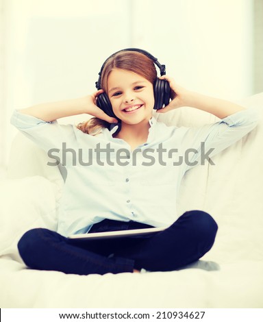 home, leisure, new technology and music concept - smiling little girl with tablet pc computer and headphones at home