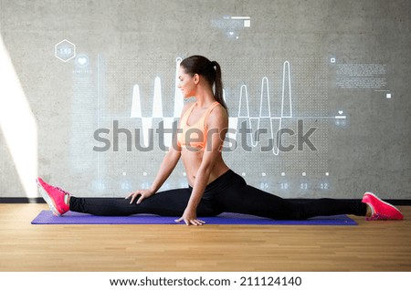 fitness, sport, training, future technology and lifestyle concept - smiling woman stretching leg on mat in gym over cardiogram projection