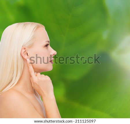 health and beauty concept - close up of clean face of beautiful young woman pointing finger to ear