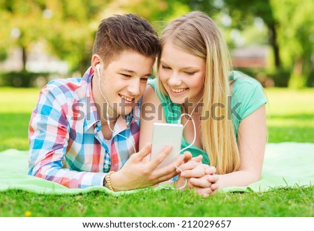 vacation, holidays, technology and friendship concept - smiling couple with smartphone and earphones making selfie in park
