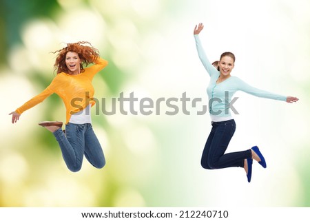 happiness, freedom, ecology, friendship and people concept - smiling young women jumping in air over green background