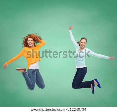 happiness, freedom, friendship, education and people concept - smiling young women jumping in air over green board background