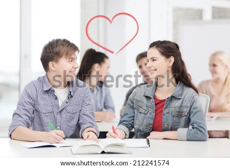 education, school and people concept - two teenagers with notebooks and book looking at each other at school