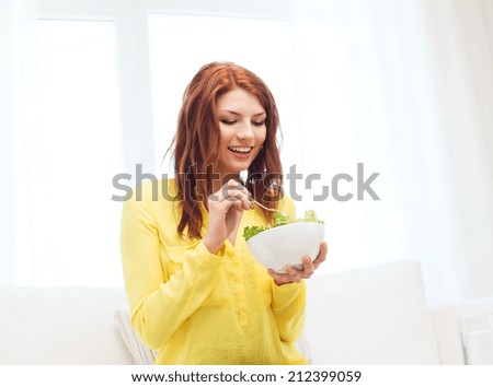 health, dieting, home and happiness concept - smiling young woman eating green salad at home