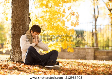 healthcare and medicine concept - ill man with paper tissue in autumn park