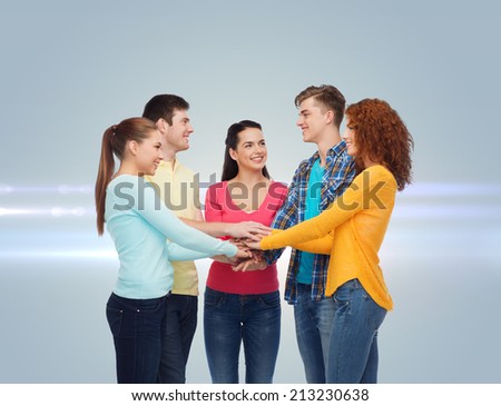 friendship, teamwork, gesture and people concept - group of smiling teenagers with hands on top of each other over gray background with laser light