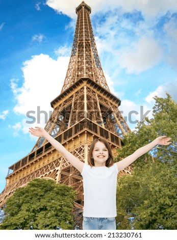 advertising, childhood, tourism, gesture and people concept - smiling girl in white t-shirt with raised arms over eiffel tower background