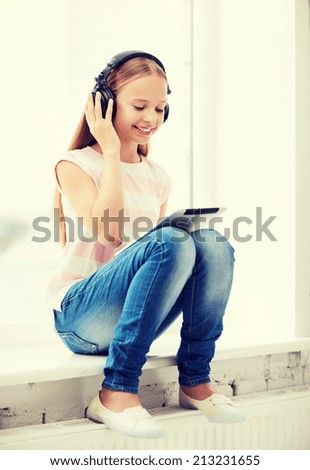 home, leisure, new technology, music concept - little girl with tablet pc and headphones at home