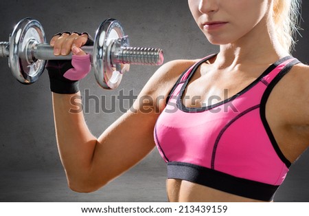 fitness, sport, exercising and people concept - close up of sporty woman with heavy steel dumbbells over concrete wall background