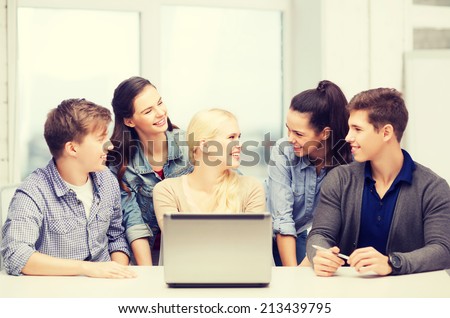 education, technology and internet concept - smiling students with laptop at school looking at each other