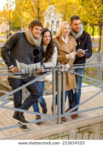 travel, people, tourism, and friendship concept - group of smiling friends with map and city guide standing on bridge in city park