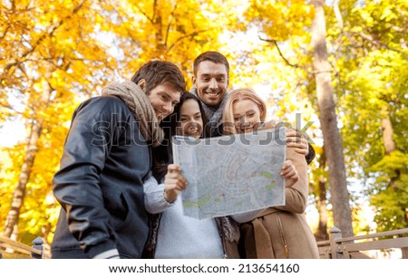 travel, vacation, people, tourism and friendship concept - group of smiling friends looking to map in city park