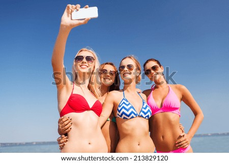 summer vacation, holidays, travel, technology and people concept- group of smiling young women on beach making selfie with smartphone over blue sky background