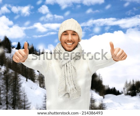 winter holidays, vacation and lifestyle concept - handsome man in warm sweater, hat and scarf showing thumbs up