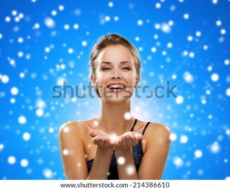 advertisement, winter holidays, christmas, people and luxury concept - laughing woman in evening dress holding something imaginary over black background over blue snowy background