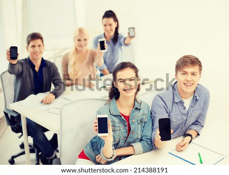education, school, technology and internet concept - smiling students showing black blank smartphone screens at school