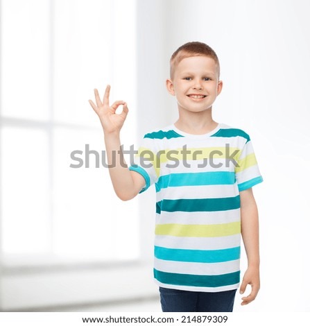 childhood, home, gesture and people concept - smiling little boy in casual clothes making ok gesture over white room background