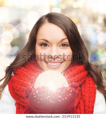 happiness, winter holidays and people concept - smiling young woman in red scarf and mittens with christmas ball over lights background
