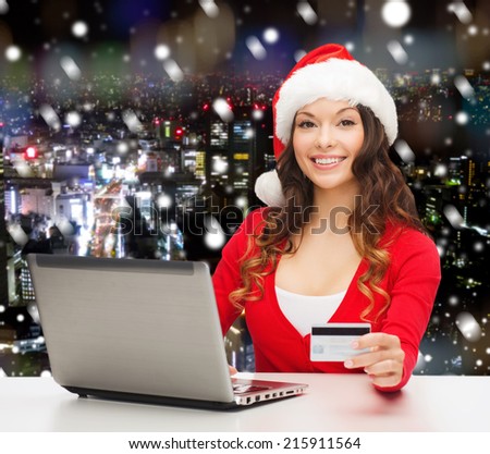christmas, holidays, technology and shopping concept - smiling woman in santa helper hat with credit card and laptop computer over snowy night city background
