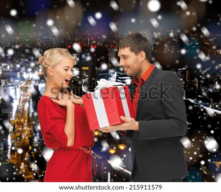 christmas, holidays, celebration and people concept - smiling man and woman with present over snowy night city background