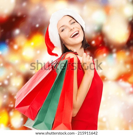 shopping, sale, gifts, christmas concept - smiling woman in red dress and santa helper hat with shopping bags