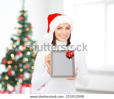 christmas, technology, present and people concept - smiling woman in santa helper hat with blank screen tablet pc computer over living room and christmas tree background