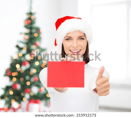 christmas, holdays, people, advertisement and sale concept - happy woman in santa helper hat with blank red card showing thumbs up gesture over living room and christmas tree background