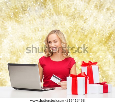 christmas, holidays, technology and shopping concept - smiling woman in red blank shirt with gift boxes, credit card and laptop computer over yellow lights background